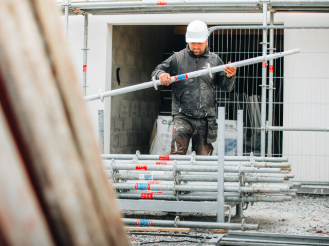 Ouvrier avec casque transporte tube sur chantier